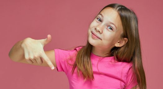 Happy child girl point with finger down at sale offer or promotion, smiling schoolgirl recommend link to subscribe on pink studio background. High quality photo